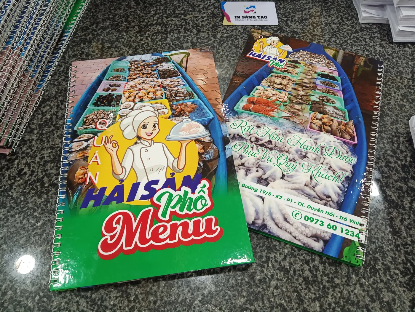 Hai cuốn menu giấy đóng lò xo đặt trên bàn tại xưởng IST